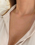 A close-up of a person's neck and upper chest wearing a layered set of delicate gold figaro link necklaces over a light cream-colored collared shirt.