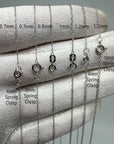 A close-up of a white fabric-covered hand displaying several white gold-tone rope chain necklace clasp options labeled by width and clasp type, with text overlays reading 0.7mm, 0.8mm, 1mm, 1.2mm and 4mm spring clasp or 5mm spring clasp