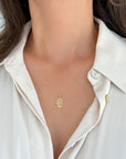 A close-up of a model wearing a delicate yellow gold hamsa hand pendant necklace over a white collared shirt.
