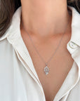 A close-up of a woman wearing a dainty white gold 0.8mm twisted rope chain necklace with a hand of Fatima pendant, styled with a cream-colored collared shirt.