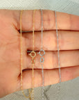 Two delicate figaro link chain necklaces, one yellow gold and one white gold, displayed on an open hand against a textured light gray background.
