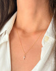 A close-up of a person wearing a delicate gold cross pendant necklace with small clear CZ stones, styled with a white collared shirt.