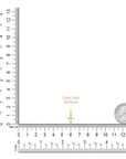 Small gold cross next to a ruler and a coin for size reference on a white background