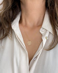 A close-up of a person wearing a delicate gold rope chain necklace with a circular pendant featuring a tree of life design, styled with a white button-down shirt.