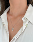 A close-up of a woman wearing a delicate white gold 0.8mm rope  necklace with a hamsa hand pendant, styled with a cream-colored collared shirt.