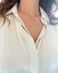 A close-up of a model wearing a dainty white gold Hamsa hand charm on 0.8mm twisted rope chain, styled with a white button-down shirt.