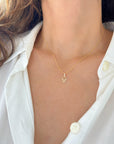 A close-up of a model wearing a delicate gold Hamsa hand necklace,  styled with a white button-down shirt.
