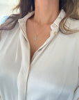 A close-up of a model wearing a delicate white solid gold Hamsa hand pendant on 0.8mm twisted rope chain, styled with a white button-down shirt.