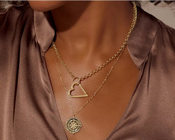 Model wearing layered 14K gold necklaces with compass pendant and open heart charm
