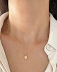 A close-up of a model wearing a delicate gold rope chain necklace with a small oval Our Lady of Grace Virgin Mary Pendant, styled with a white collared shirt.