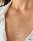 A close-up of a person's neck and upper chest wearing layered yellow 10k gold twisted rope chain necklaces at different lengths, with printed size labels reading 16", 18", 20", 22", 24" and 1mm.